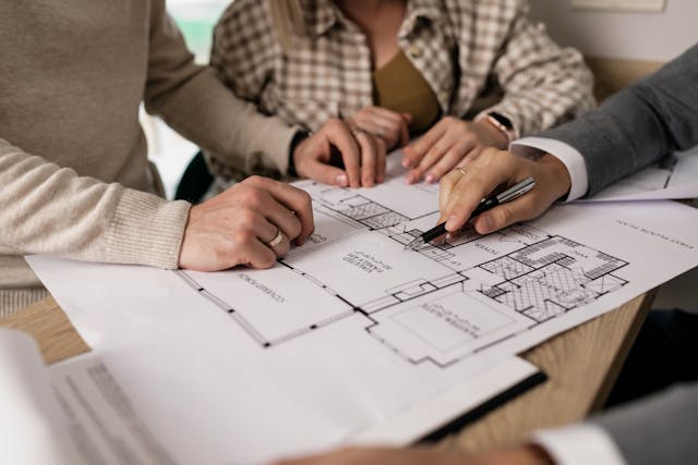three people going over a house blueprint three people going over a house blueprint